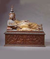 A carvedand painted teakwood figure of a Buddha, reclining on top of a chest